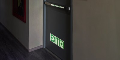 A clear shot of a NFPA photoluminescent exit sign glowing brightly in a dimly lit hallway.