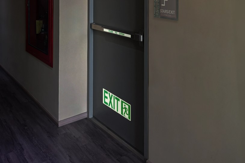 A clear shot of a NFPA photoluminescent exit sign glowing brightly in a dimly lit hallway.