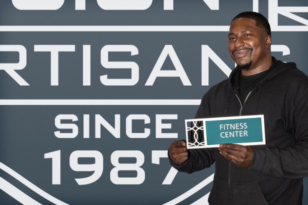 EvacuationPlans.com artisan Eric Reynolds holding a Diverge Fitness Center sign, showcasing bold contrast and dimensional design that enhances visibility in emergency egress routes.