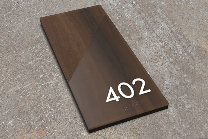 A modern ADA-compliant room number sign in the Incline Sign Style, featuring a diagonal two-tone wood design with raised tactile numbers and Grade 2 braille reading ‘402,’ displayed on a neutral textured surface.