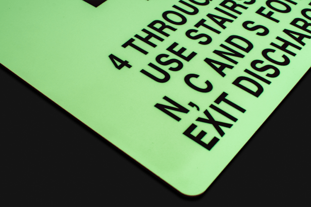 Photoluminescent sign glowing in low light displaying emergency exit instructions.