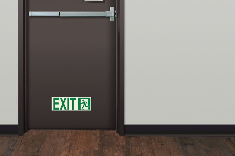 Photoluminescent Emergency Exit Sign (Left) mounted low on door marking emergency egress path.