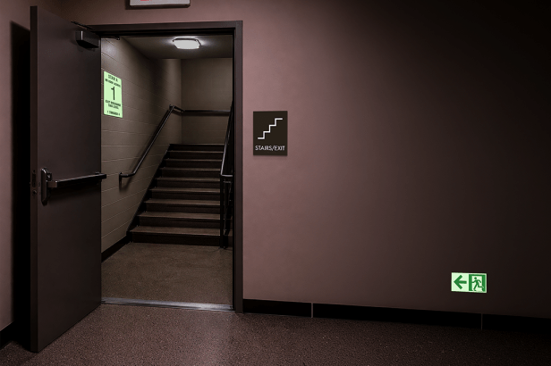 Photoluminescent Emergency Exit Directional Sign (Left) mounted low on wall directing occupants to stairwell exit.